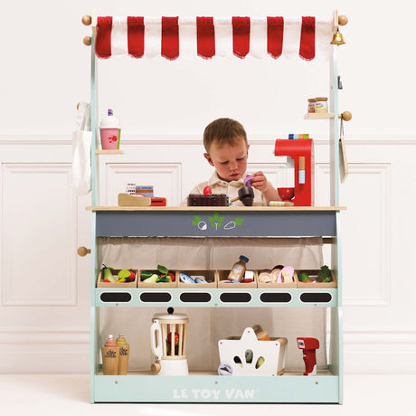 Young boy playing behind a stocked wooden market stall toy set.