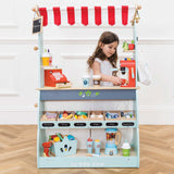 Young girl playing behind a fully stocked Le Toy Van wooden market stall and café set on a herringbone floor.