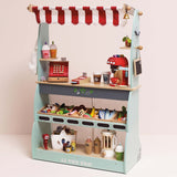 Wooden play market stall filled with toy groceries, cash register, and coffee maker on shelves.