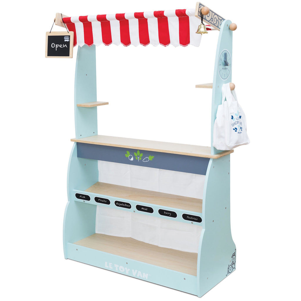 Toy market stall with red and white striped canopy and open sign. Features shelves labeled with food categories, a bell, and a hanging bag. Bright and playful.