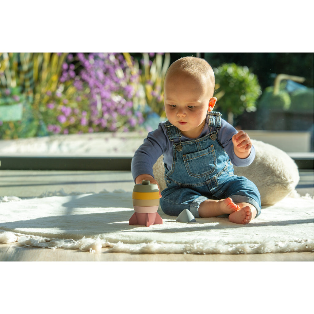 A soft silicone stacking toy in earthy tones, shaped like a rocket, designed to encourage sensory exploration and fine motor skills.