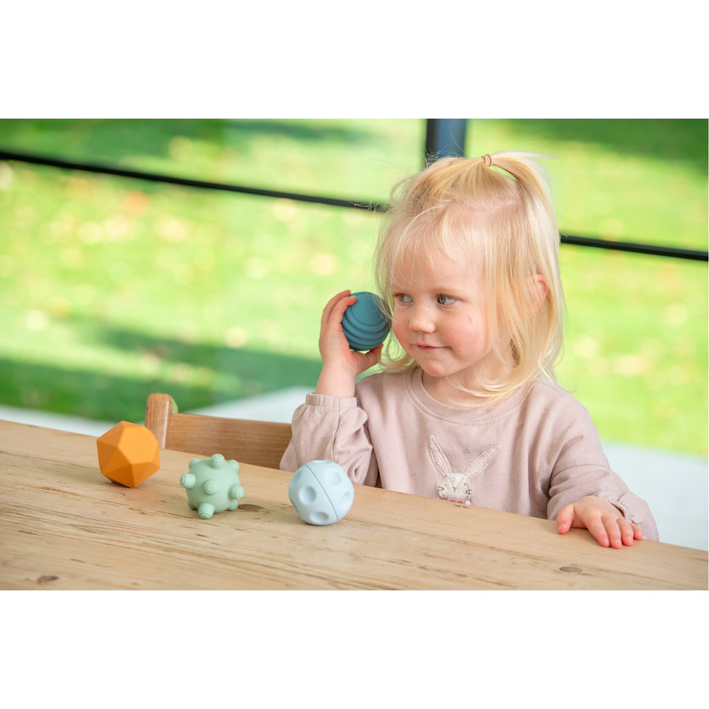 A set of soft silicone balls in neutral tones, featuring a textured surface to encourage tactile exploration and sensory development in young children.