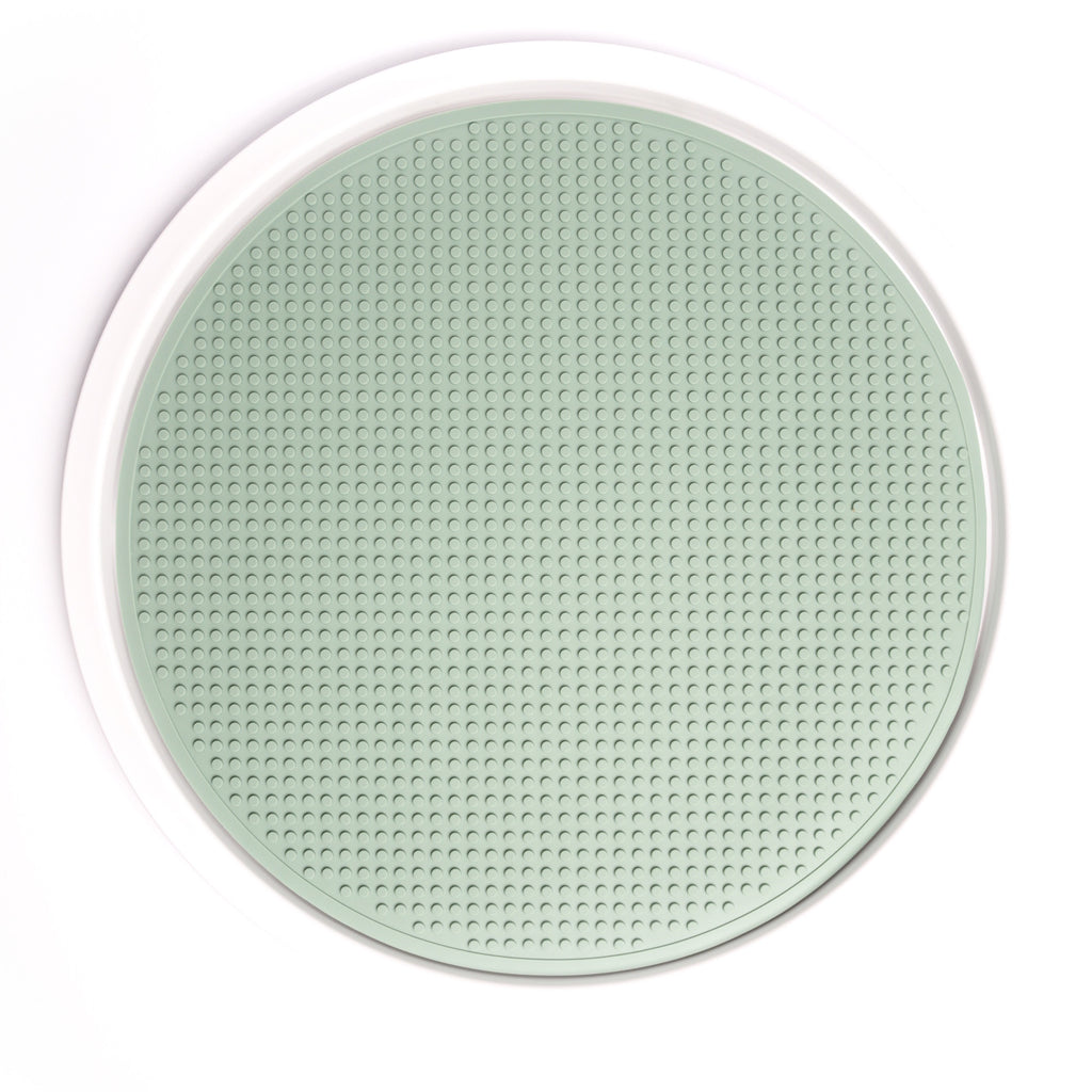 A round, smoke green silicone mat with a textured, raised dot pattern is surrounded by a white circular rim. The design conveys a simple, modern aesthetic.