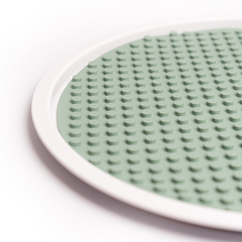 A round, smoke green silicone mat with a textured, raised dot pattern is surrounded by a white circular rim. The design conveys a simple, modern aesthetic.