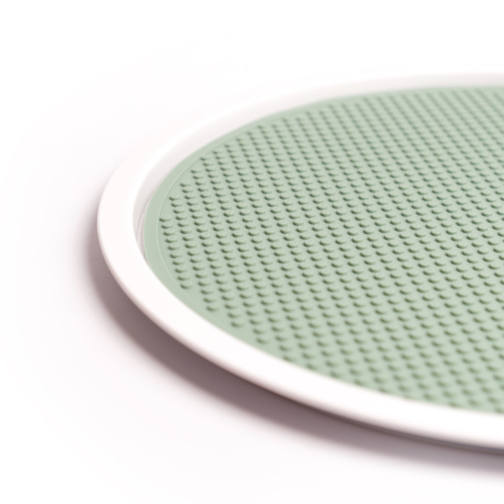 A round, smoke green silicone mat with a textured, raised dot pattern is surrounded by a white circular rim. The design conveys a simple, modern aesthetic.