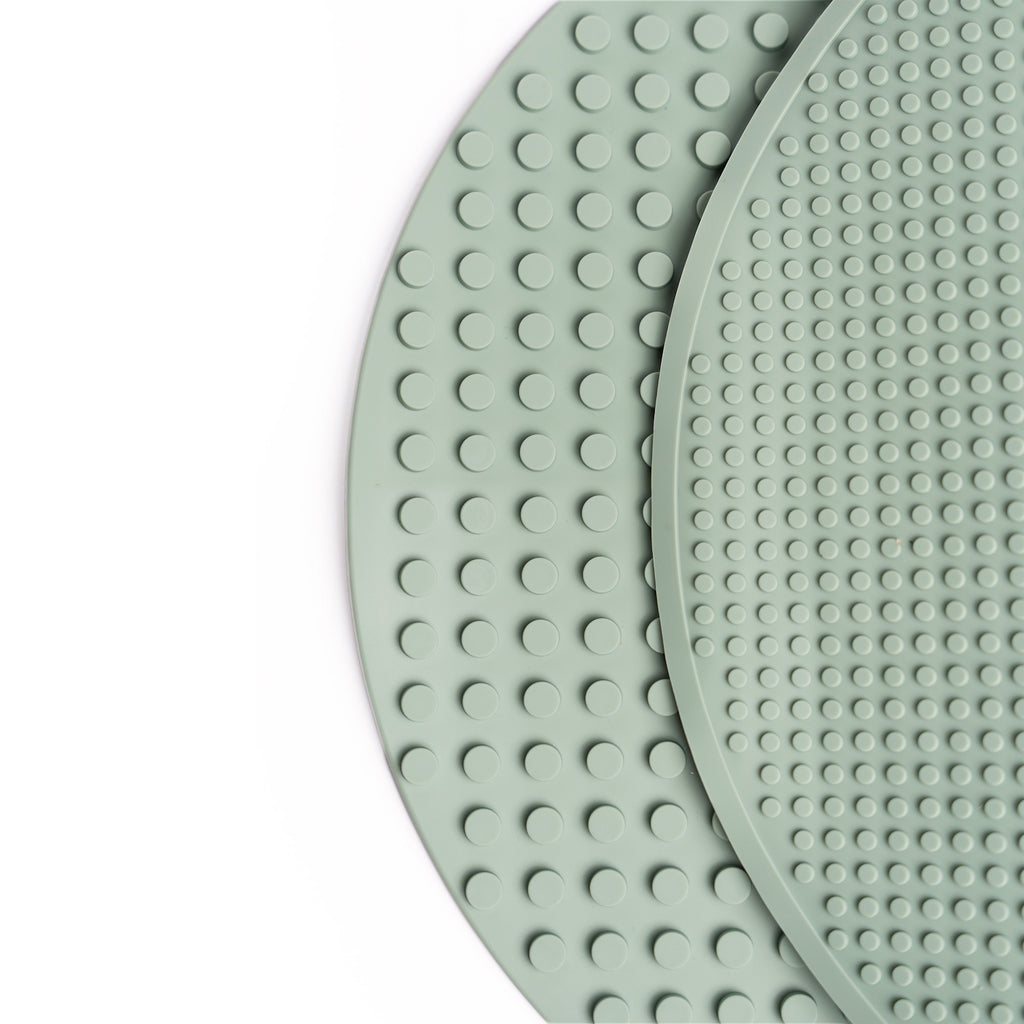 A round, smoke green silicone mat with a textured, raised dot pattern is surrounded by a white circular rim. The design conveys a simple, modern aesthetic.