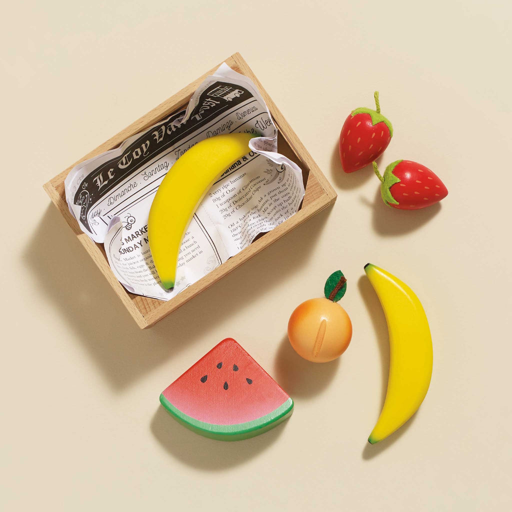 Wooden crate of colorful toy fruits, including bananas, strawberries, orange, and a watermelon slice. Bright, playful, and neatly arranged.