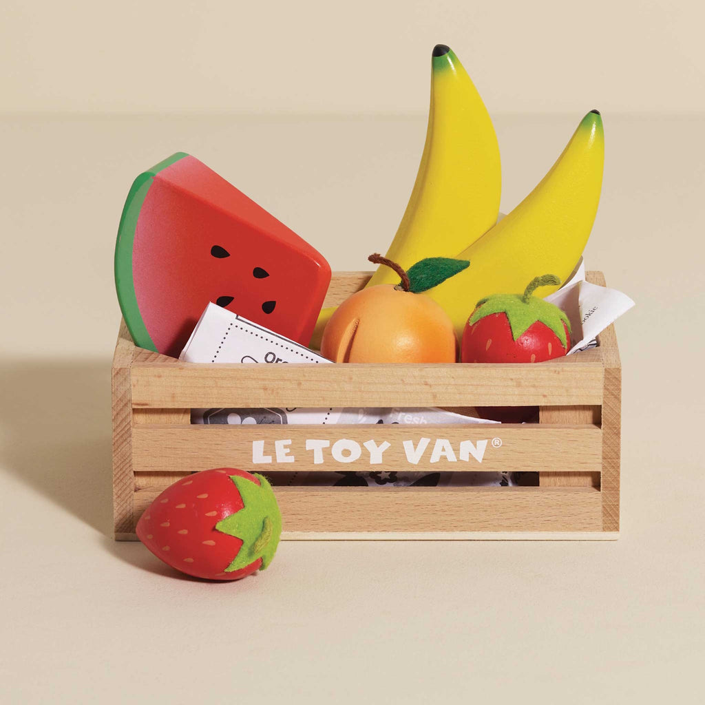 Wooden crate of colorful toy fruits, including bananas, strawberries, orange, and a watermelon slice. Bright, playful, and neatly arranged.