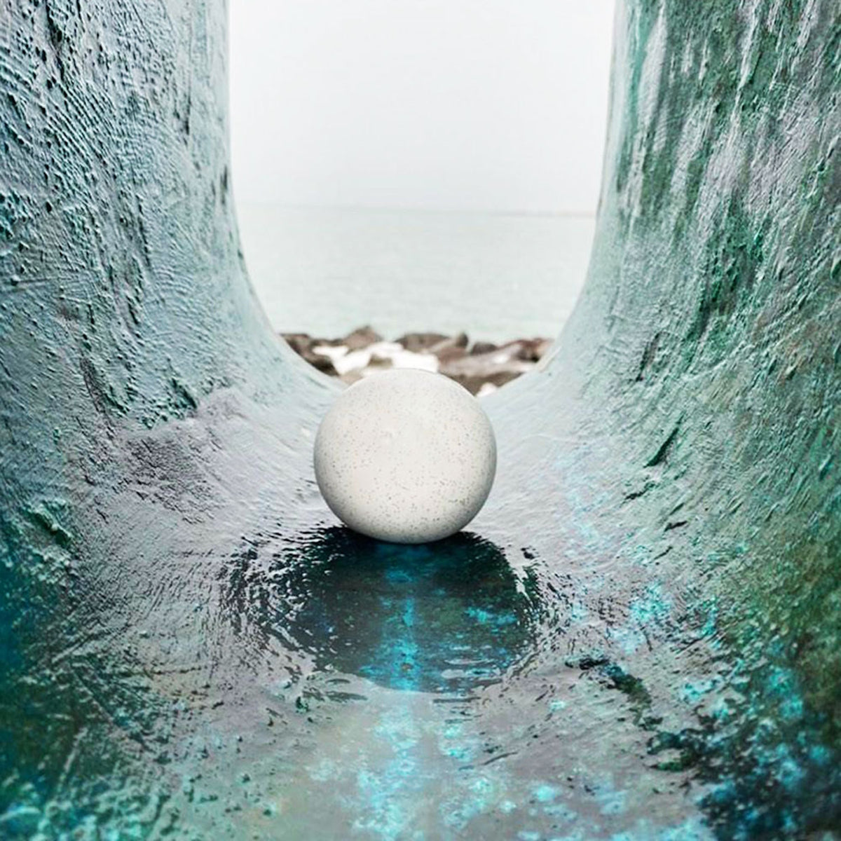 White crunch snowball stress toy sitting on a teal textured surface with a blurred ocean background for sensory play.