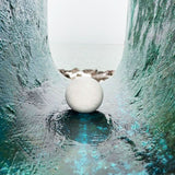 White crunch snowball stress toy sitting on a teal textured surface with a blurred ocean background for sensory play.