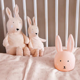 Stuffed bunny toys and a soft bunny lamp sit on a crib mattress with pale bedding. The scene is cozy and serene, emitting a warm, gentle vibe.