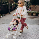 Toddler pushing a Sollie Stroller Rose toy pram with plush dolls inside.
