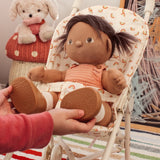 A cloth doll with pigtails sitting in a toy stroller with a rainbow-patterned seat liner.