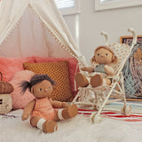 Two plush dolls in a playroom, one sitting on a rug and one in a rainbow-patterned toy stroller.