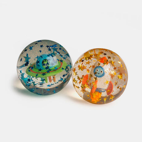 Two clear bouncy balls on a white background; one with a green alien spacecraft and blue stars, the other with an orange smiling robot and gold stars. Playful tone.