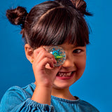 A smiling child holds a clear star-filled toy in front of one eye against a bright blue background. The joyful expression conveys playfulness.