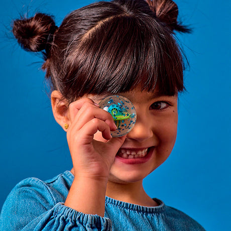 A smiling child holds a clear star-filled toy in front of one eye against a bright blue background. The joyful expression conveys playfulness.