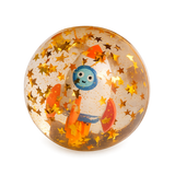 A transparent ball contains a smiling cartoon rocket surrounded by golden star confetti. The playful scene exudes a whimsical, space-themed charm.