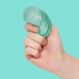 A hand is squeezing a translucent, green gel stress ball against a solid turquoise background, conveying a sense of tension relief and focus.