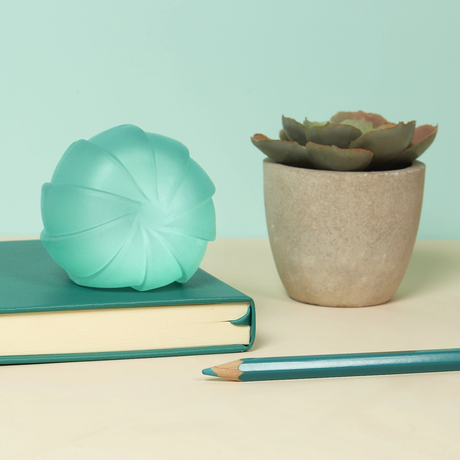 A textured teal sphere rests on a teal book beside a potted succulent on a beige surface. A matching teal pencil lies nearby. Calm, coordinated aesthetic.