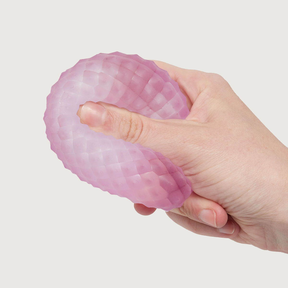 A hand squeezing a soft, textured, pink stress ball with a honeycomb pattern against a plain white background, conveying a sense of relief and relaxation.