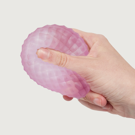 A hand squeezing a soft, textured, pink stress ball with a honeycomb pattern against a plain white background, conveying a sense of relief and relaxation.
