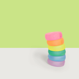 Stacked Speks Loop Gump memory gel stress rings in a rainbow of colors against a green background.