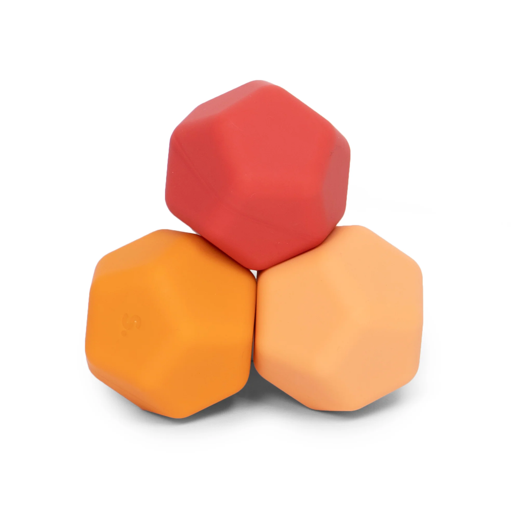 Three stacked, geometric juggling balls in red, orange, and peach colors, arranged in a triangle. The setup conveys a playful, balanced tone.