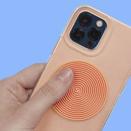 A hand rubs a circular grooved orange silicone sensory sticker attached to the back of a phone.