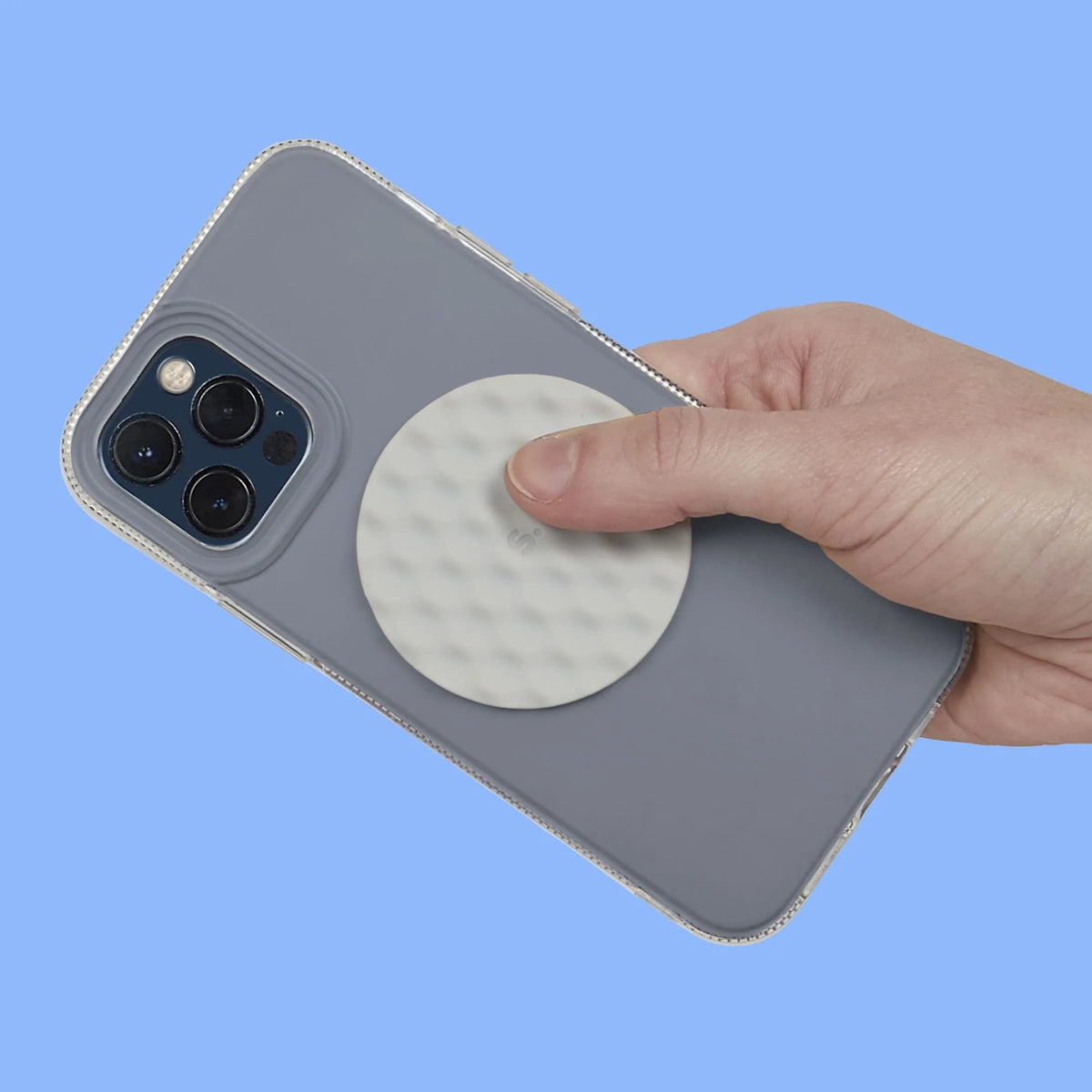 Hand holding a grey phone case with a circular light grey textured silicone sensory sticker attached.