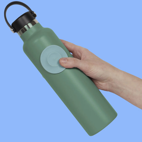Hand holding a green water flask with a circular light blue silicone sensory sticker attached.