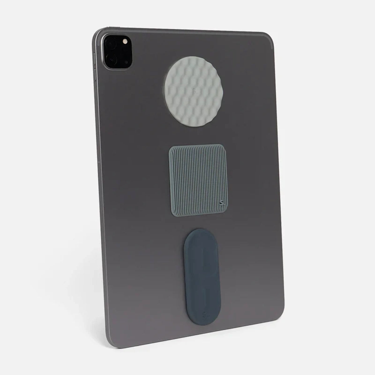 Grey tablet standing upright with three different textured silicone sensory stickers applied to its back.