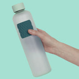 Hand holding a light blue water bottle with a dark green textured sensory sticker attached.