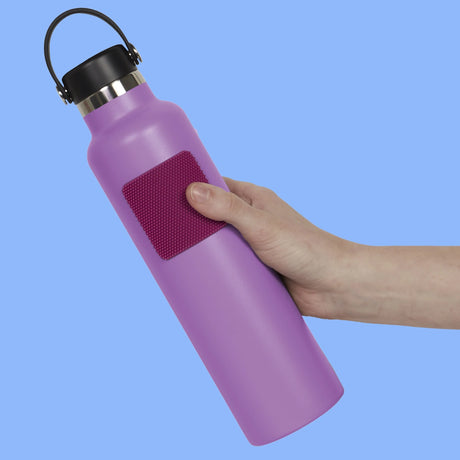 Hand holding a purple water bottle with a square purple textured silicone sensory sticker attached.