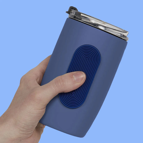 A hand holds a blue tumbler featuring an oval grooved silicone sensory sticker.