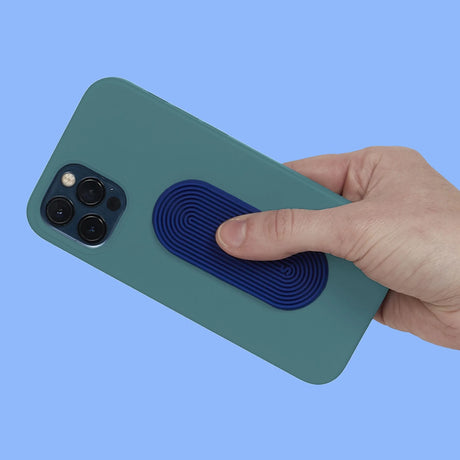 A hand rubs an oval blue grooved silicone sensory sticker attached to a green phone case.