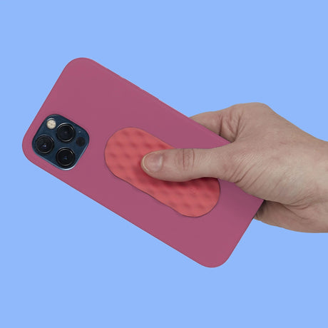 A hand rubs an oval pink textured silicone sensory sticker attached to a pink phone case.