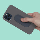 Hand holding a dark grey phone case with an oval dark grey silicone sensory sticker attached.