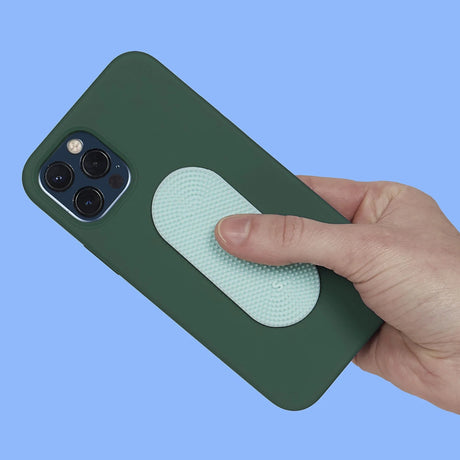 Hand holding a dark green phone case with an oval light green textured sensory sticker attached.