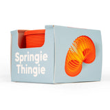 Box of a toy named "Springie Thingie," featuring a colorful orange and yellow spring graphic, partially visible inside. Playful and fun vibe.