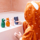 A child in an orange hooded bathrobe plays with four animal-shaped toys on a bathtub ledge. The toys are green, orange, pink, and blue, evoking a playful mood.