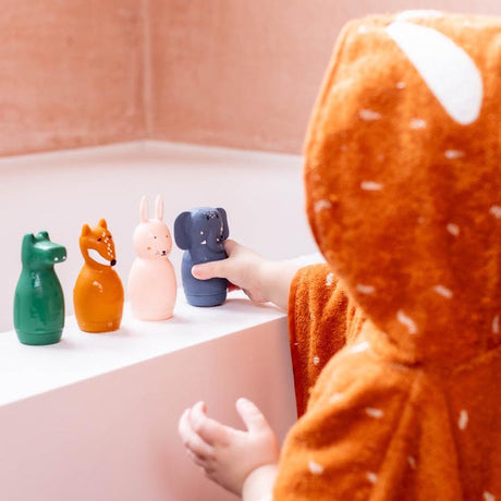 A child in an orange hooded bathrobe plays with four animal-shaped toys on a bathtub ledge. The toys are green, orange, pink, and blue, evoking a playful mood.