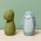 Two cute, egg-shaped rubber toys, a green dinosaur and a blue shark, standing on a light wood surface.