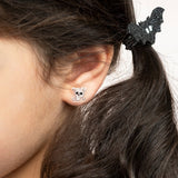 Close-up of a child wearing a skull sticker earring and a black glitter bat hair accessory.