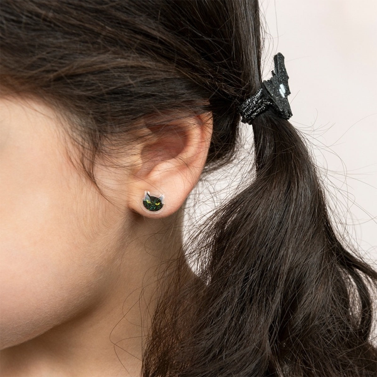 Close-up of a child wearing a black cat sticker earring and a glittery bat hair accessory.