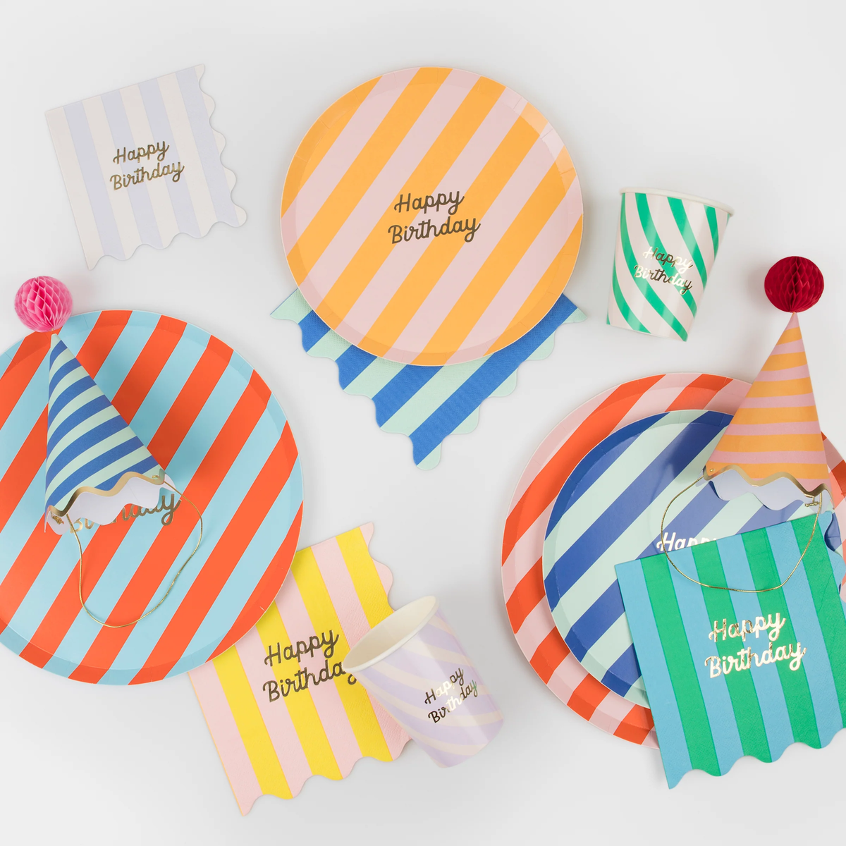 Colorful striped birthday party tableware set including plates, cups, napkins, and party hats.