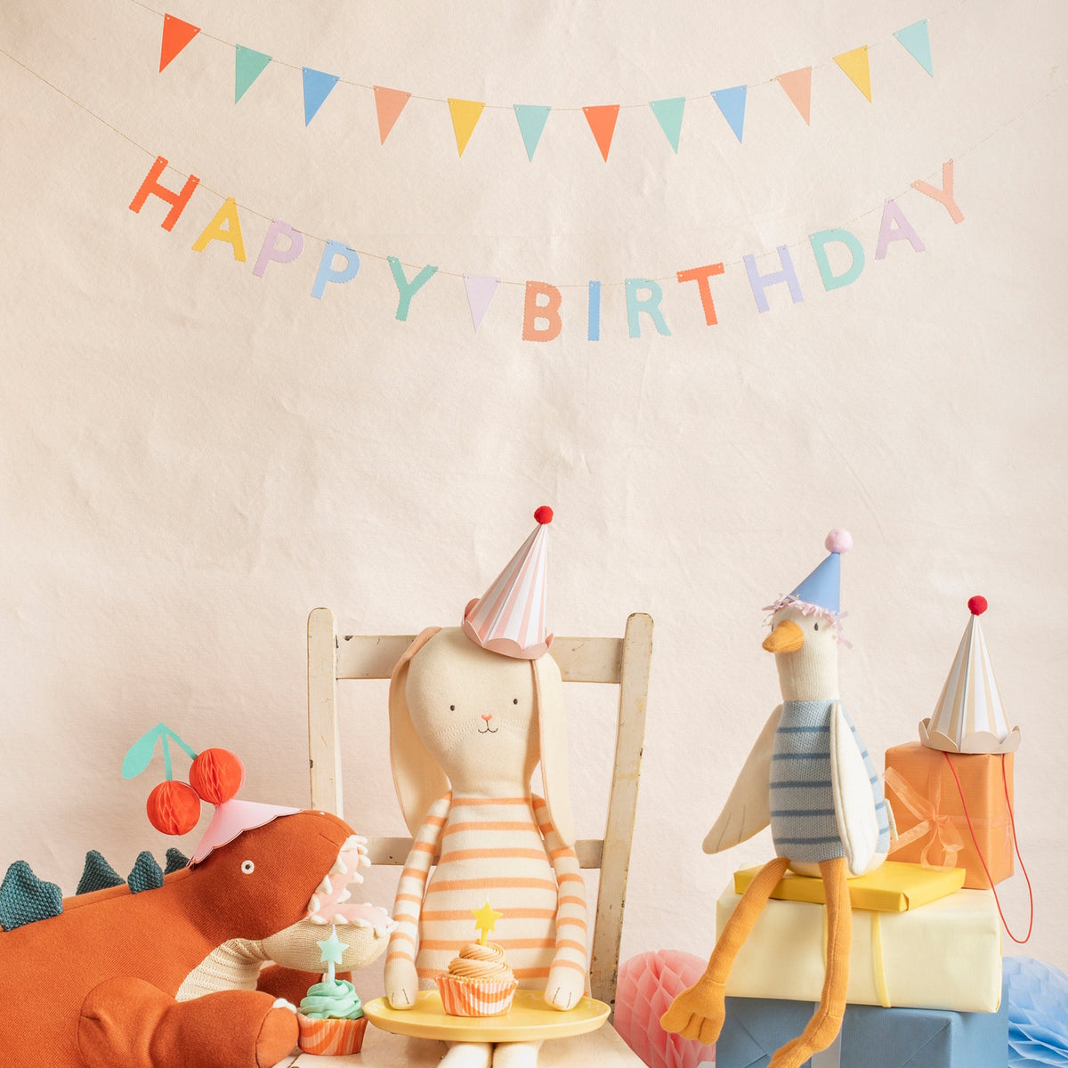 Stuffed animal toys wearing party hats celebrating a birthday with a cupcake and a Happy Birthday banner.