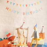 Stuffed animal toys wearing party hats celebrating a birthday with a cupcake and a Happy Birthday banner.