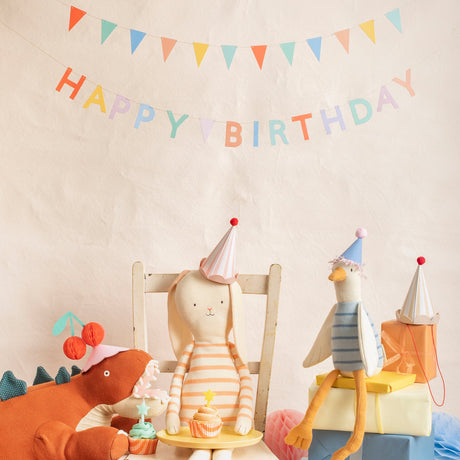 Stuffed animal toys wearing party hats celebrating a birthday with a cupcake and a Happy Birthday banner.