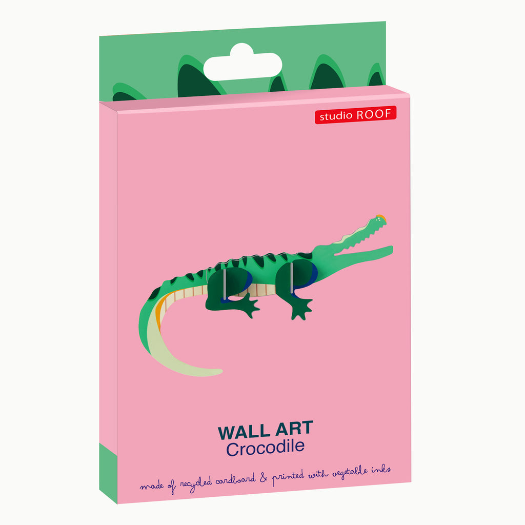Packaging for Studio Roof crocodile wall art. Features a playful green crocodile illustration on a pink background. Text highlights eco-friendly materials.